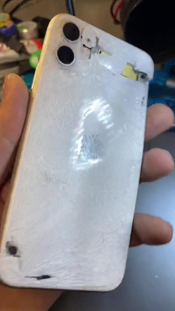 Geöffnetes iPhone 11 mit beschädigtem Rückglas in der Hand des Technikers